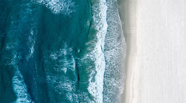 Aerial view of sea waves rolling on an empty white beach