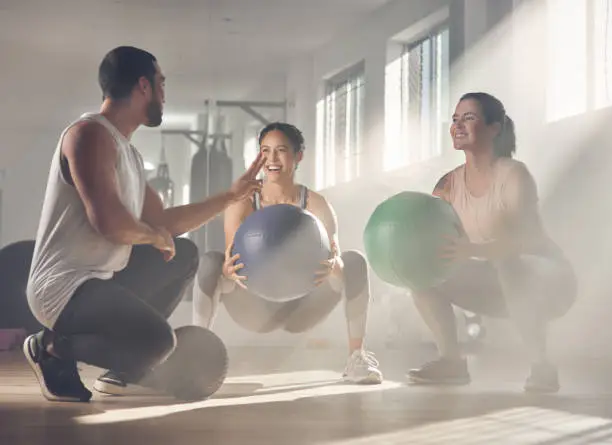 Shot of two women using fitness balls while working out with their trainer