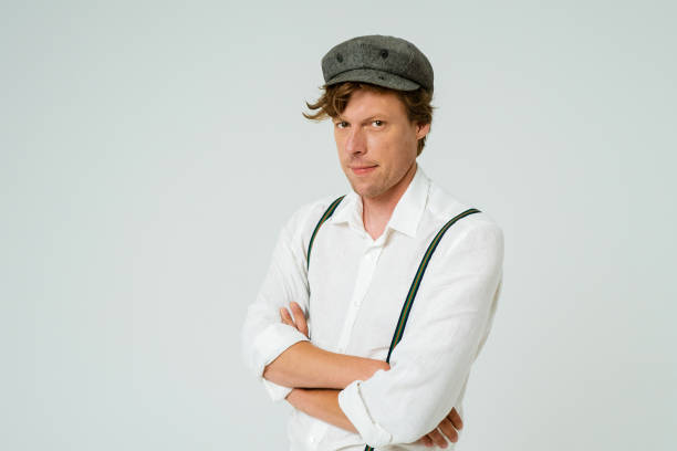 istock Hipster man posing with hands folded dressed in white shirt and grey wool cap isolated on white background. Copy space at left side 1290663457