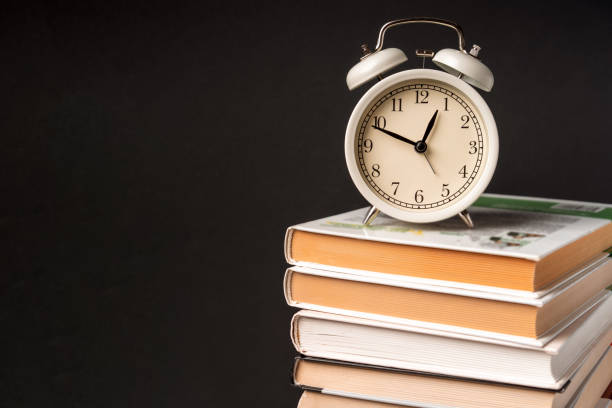 istock The alarm clock stands on a stack of books on a black background. Training concept and preparation for work 1290663909