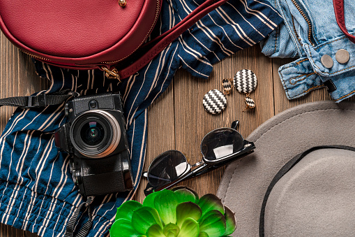 Women's clothing and travel accessories on a natural wooden background top view. Modern and casual outfit, the concept of preparing for a vacation