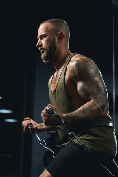 Tattooed bodybuilder doing low cable crossover exercise. Portrait of muscular tattooed bodybuilder doing low cable crossover exercise. Side crop of man with perfect body training chest in gym in dark atmosphere. Concept of bodybuilding. chest tattoo men stock pictures, royalty-free photos & images