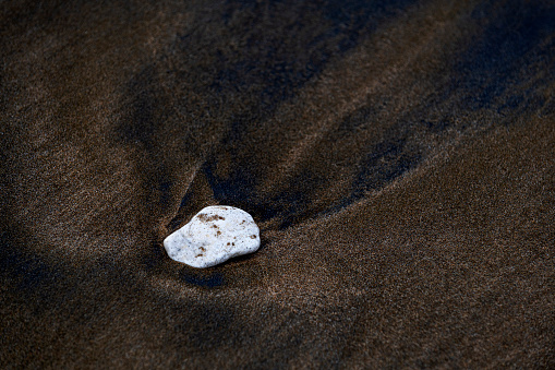 A small white stone on brown sand on the seashore in Turkey.