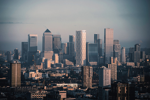 Aerial panoramic view of The City of London cityscape skyline with metropole Canary Wharf financial district modern skyscrapers during sunrise with illuminated buildings and cloudy sky in London, UK