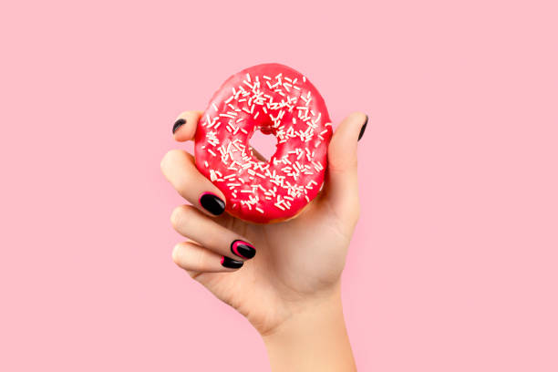 istock Womans hand holding colorful donut over pink background 1290671936