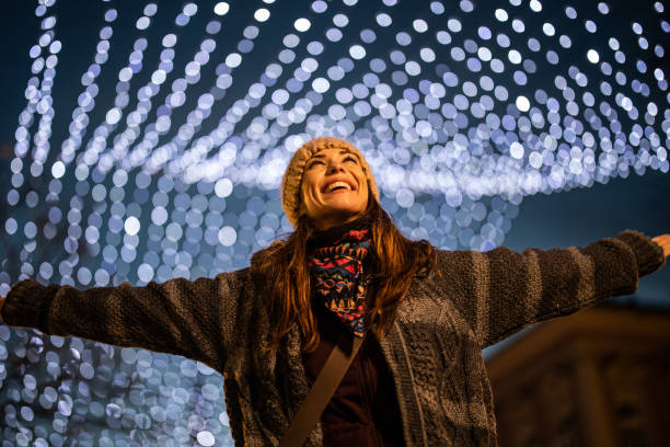 Young smiling woman standing on well decorated town square with christmas lights and spinning Beautiful young smiling woman standing on well decorated town square with christmas lights and spinning with outstretched arms christmas excitement stock pictures, royalty-free photos & images