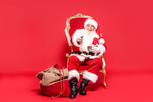 Full size photo of real santa claus with popcorn and remote control in hand, relaxing before Christmas time. Red studio background.