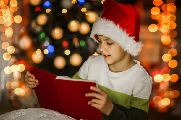 istock Boy, reading a book in front of a Christmas tree. 1290677296