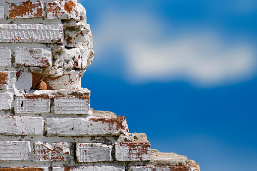 Old broken wall of white brick on a background of blue sky. Focus on the wall, background blurred.