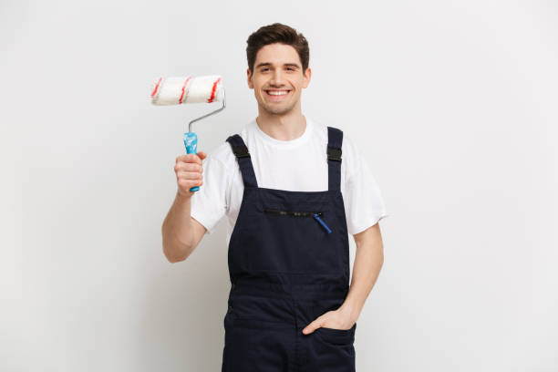istock Smiling male builder with arm in pocket holding paint roll 1290682057