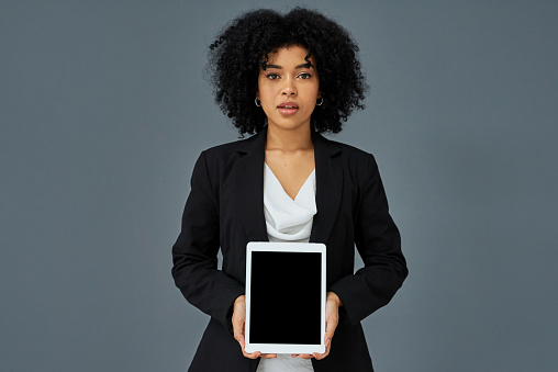 Shot of a young businesswoman holding a digital tablet with a blank screen against a grey studio background
