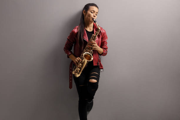 istock Beautiful woman leaning on a gray wall and playing sax 1290685413
