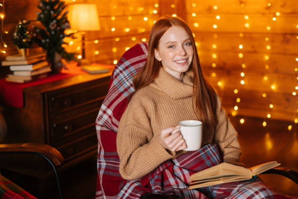 istock Happy young woman drinking hot coffee from cup and reading book while sitting at rocking armchair. 1290685422