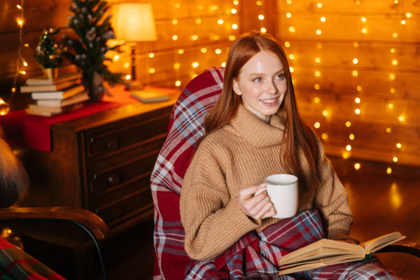 istock Happy young woman drinking hot coffee from cup and reading book while sitting at rocking armchair. 1290685631