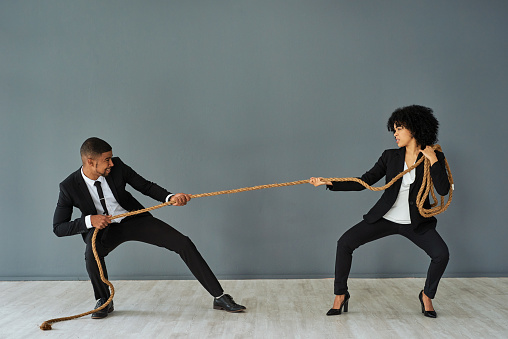 Shot of young a businessman and businesswoman playing tug of war against a grey studio background