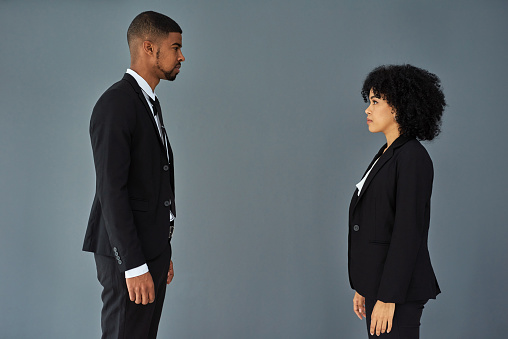 Shot of young businessman and businesswoman standing face to face against a grey studio background