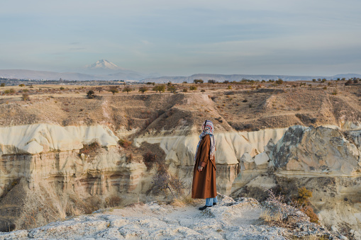 Young Caucasian woman in headscarf standing and looking at caves in  Cappadocia in Turkey