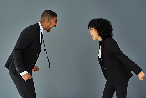 Studio shot of a young businessman and businesswoman yelling at each other against a grey background