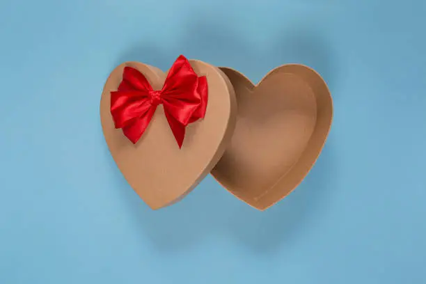 Open gift empty craft box in the shape of a heart with a red bow on a blue background. Gift wrapping for Valentine's Day.