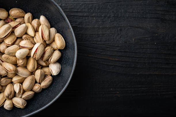 Shelled, unsalted pistachios, on black wooden table, top view with space for text