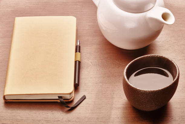 copy book, pen, teapot and cup of tea on a wooden desk
