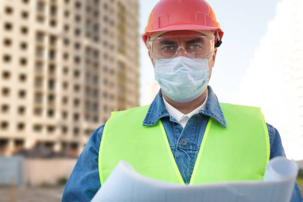istock Engineer in red protective helmet and medical mask with blueprint  at construction site 1290696376