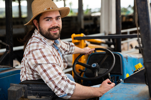 Portrait of smiling young bearded farmer sitting on small farm tractor