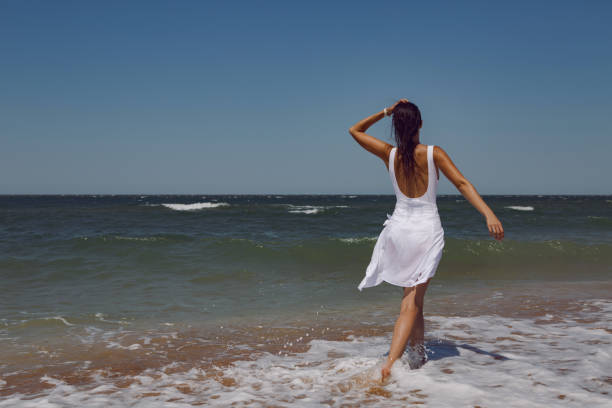 istock woman in a white bathing suit and a straw hat stands on an empty sandy beach 1290700865