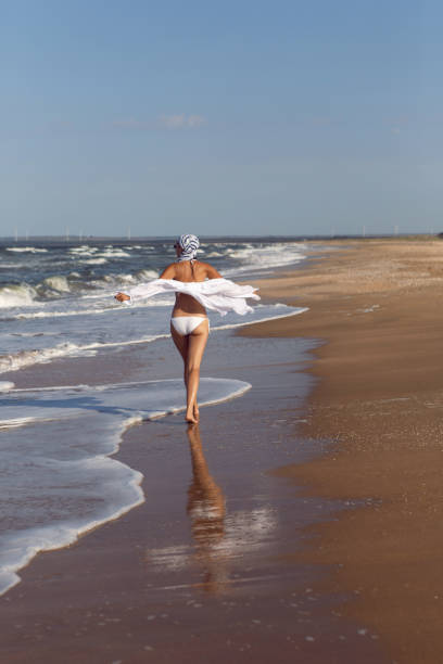 istock woman run in a white bathing suit and hat sunglasses on an empty sandy beach 1290701039