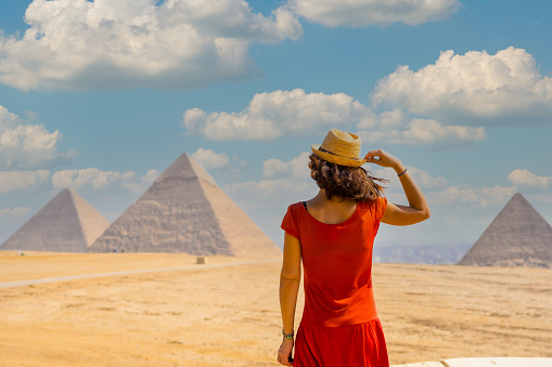 A young tourist in a red dress looking at the Pyramids of Giza, the oldest Funerary monument in the world. In the city of Cairo, Egypt