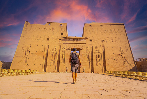A young tourist entering the Temple of Edfu in the city of Edfu at sunset, Egypt. On the banks of the River Nile, geco-Roman construction, temple dedicated to Huros