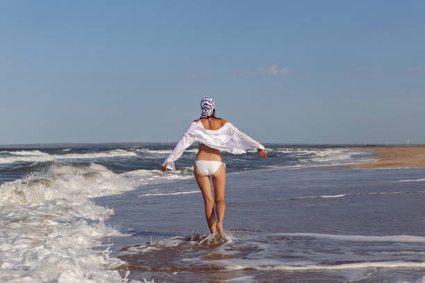 istock woman run in a white bathing suit and hat sunglasses on an empty sandy beach 1290702109