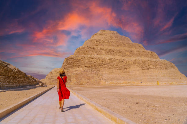 A young tourist in a red dress at the Stepped Pyramid of Djoser at sunset, Saqqara. Egypt. The most important necropolis in Memphis. The first pyramid in the world stock photo