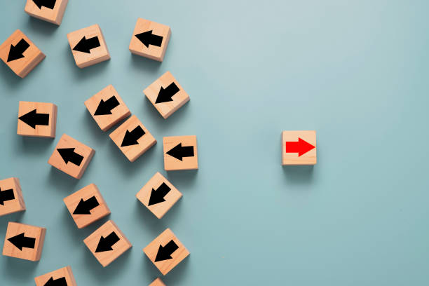 Different thinking and Business and technology disruption concept. Red arrow on wooden block is opposite direction with black arrows on blue background.