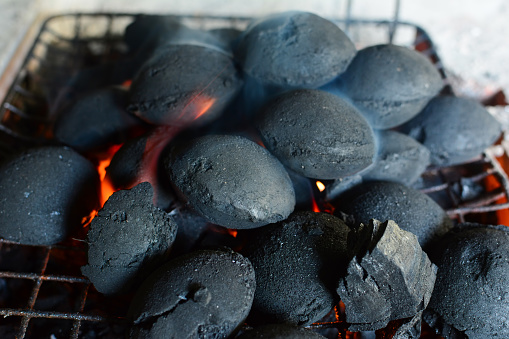Pile of round briquettes of charcoal on grill, the fire just lit, preparation for  barbeque has just started, horizontal orientation, close up view