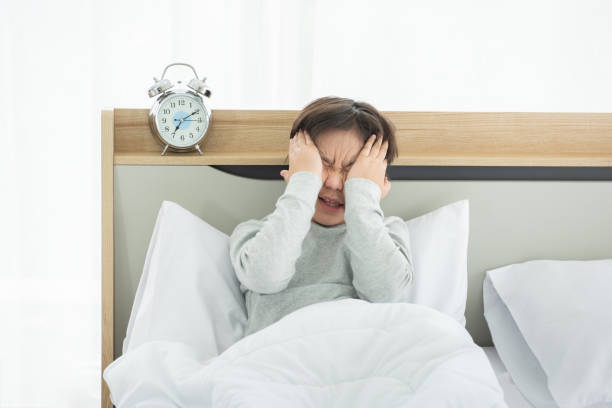 Asian boy suffering from sleep deprivation with alarm clock in bedroom Asian boy suffering from sleep deprivation with alarm clock in bedroom asian child wake up stock pictures, royalty-free photos & images
