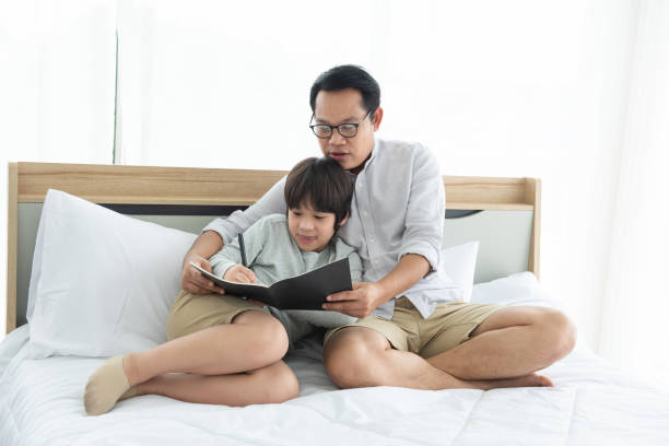 istock Father and Asian boy writing on book,lying on bed at home. 1290709761