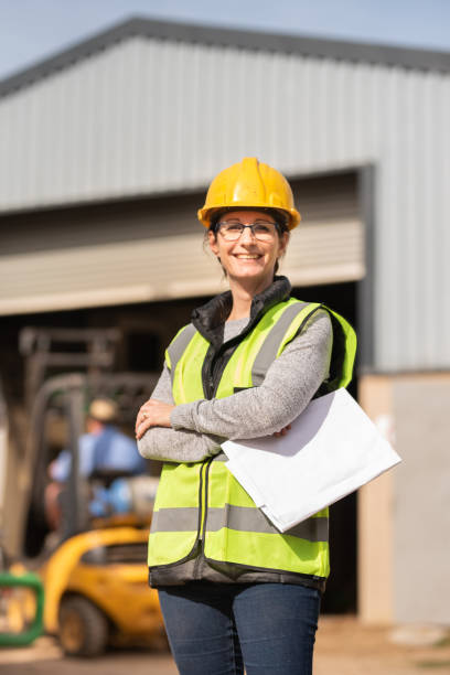 istock Smiling female engineer standing with blueprints on a building site 1290717457