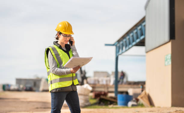 female engineer talking on the phone and reading blueprints on a worksite - female construction telephone building contractor imagens e fotografias de stock
