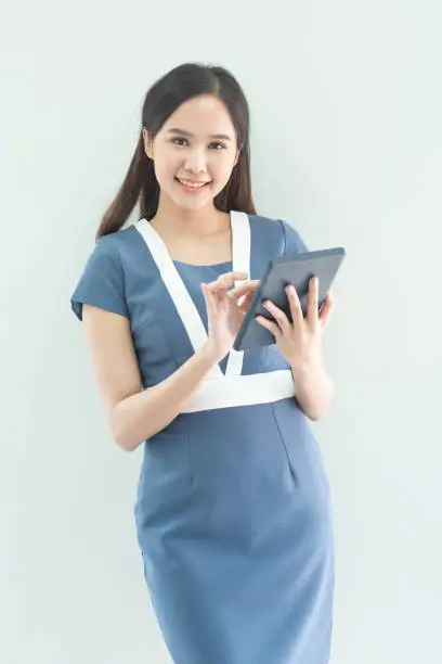 Asian woman with a tablet computer. Asian businesswoman using digital tablet computer, leaning against a grey wall.