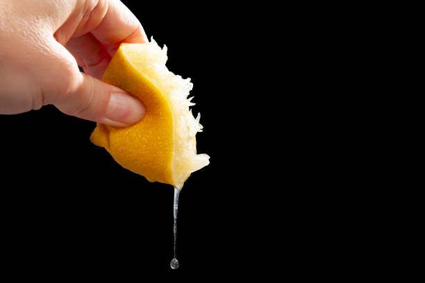 Woman squeezing lemon juice against black background. stock photo