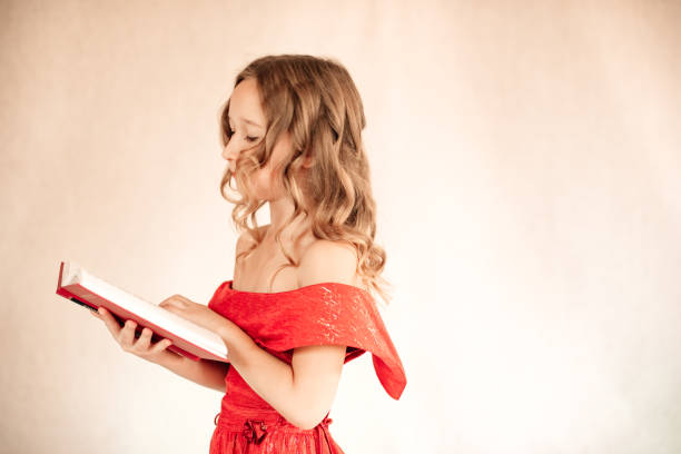 A little girl with curls in a red dress is reading a book in the background, a plain white background. Knowledge and study concept.