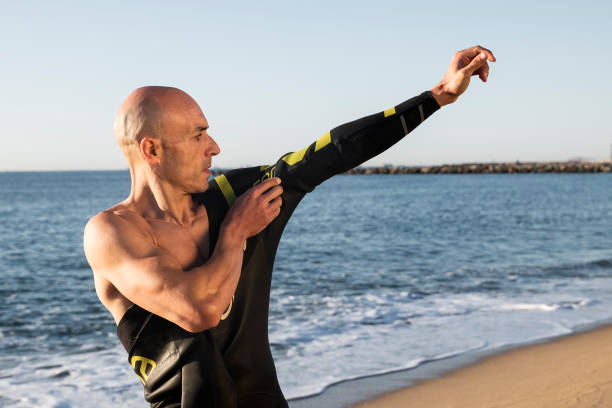 Swimmer putting on his wetsuit. Sand, beach, neoprene.