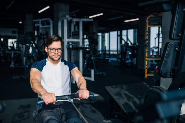 istock Gym workout. Young concentrated muscular man exercising on rowing machine. 1290725296