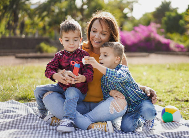 beautiful latin mother enjoy playful time with twin sons in nature park - children and soap bubbles - family love - life events laughing women latin american and hispanic ethnicity imagens e fotografias de stock