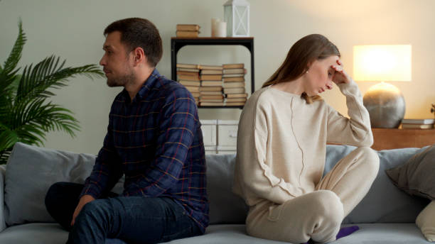 Angry couple sit separate on couch ignore avoid talking after family fight misunderstanding. Unhappy spouses man and woman think of divorce or breakup stock photo