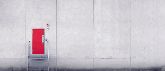 Steps leading up to a red door with security equipment in a large concrete industrial building.