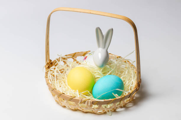istock Easter eggs and bunny in a basket isolated on white background. 1290741916