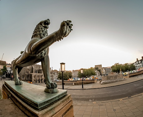 Wide angle fisheye close up of one of the lion statues outside County Hall in the city of Norwich, Norfolk. In the distance is the outdoor market and the Guildhall