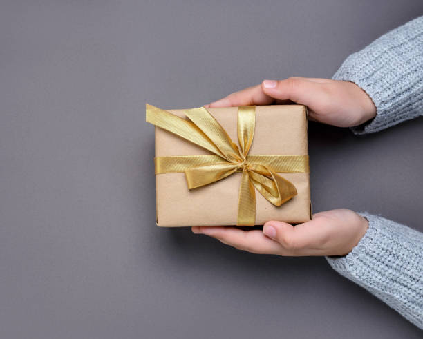 istock Hands holding gift box with a gold ribbon on a gray background 1290746191